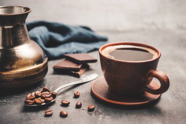 Kil fincanda sade kahve, Türk jezve kahve demliği, çikolata parçaları ve koyu arkaplanda kaşık kahve çekirdekleri..