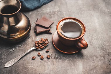 Kil fincanda sade kahve, Türk jezve kahve demliği, çikolata parçaları ve koyu arkaplanda kaşık kahve çekirdekleri..