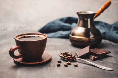 Kil fincanda sade kahve, Türk jezve kahve demliği, çikolata parçaları ve koyu arkaplanda kaşık kahve çekirdekleri..