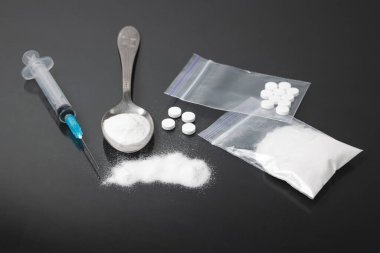 Karanlık arka planda ağır yasadışı uyuşturucular, kokain veya eroin beyaz toz, beyaz haplar, şırınga ve kaşık. Uyuşturucu bağımlılığı ve bağımlılık kavramı.