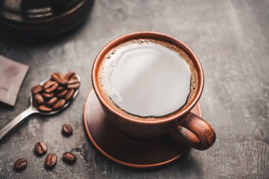 Kil fincanda sade kahve ve koyu arkaplanda kaşık kahve çekirdekleri. .