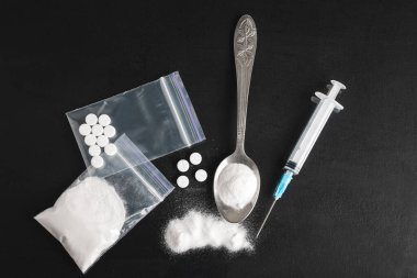 Karanlık arka planda ağır yasadışı uyuşturucular, kokain veya eroin beyaz toz, beyaz haplar, şırınga ve kaşık. Uyuşturucu bağımlılığı ve bağımlılık konsepti, üst bakış.