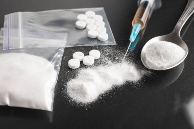 Karanlık arka planda ağır yasadışı uyuşturucular, kokain veya eroin beyaz toz, beyaz haplar, şırınga ve kaşık. Uyuşturucu bağımlılığı ve bağımlılık kavramı.