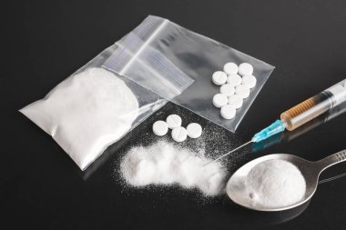 Karanlık arka planda ağır yasadışı uyuşturucular, kokain veya eroin beyaz toz, beyaz haplar, şırınga ve kaşık. Uyuşturucu bağımlılığı ve bağımlılık kavramı.