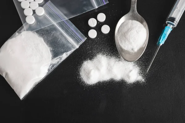Karanlık arka planda ağır yasadışı uyuşturucular, kokain veya eroin beyaz toz, beyaz haplar, şırınga ve kaşık. Uyuşturucu bağımlılığı ve bağımlılık konsepti, üst bakış.