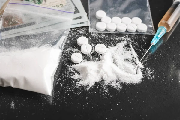 stock image Drugs on dark background, cocaine or heroin white powder, white pills, syringe with a dose and us dollar cash. Drug abuse and addiction concept.