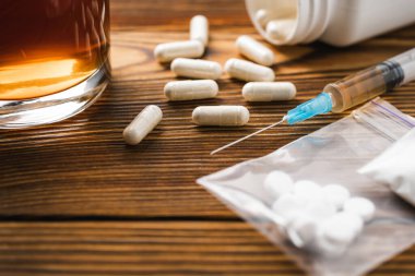 Beyaz haplar, uyuşturucu içeren şırınga, narkotik, ahşap bir masada alkollü içki bardağı, yakın çekim. Bağımlılık ve kötü alışkanlıklar kavramı.