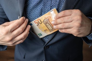 İyi giyimli adam ceketinin cebine bir sürü para koyar, Euro banknotları, Avrupa Birliği 'nin kağıt para birimi..