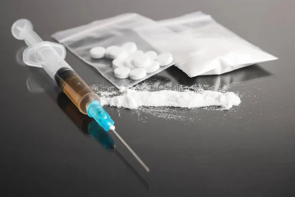 Stock image Drugs on dark background, cocaine or heroin white powder, white pills, syringe with a dose and us dollar cash. Drug abuse and addiction concept.