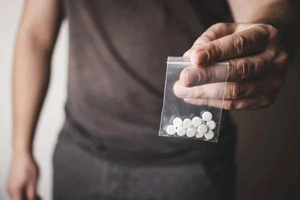 stock image Man's hand holds transparent plastic packet with white pills lsd, drug dealer selling drugs. Drug abuse and addiction concept.