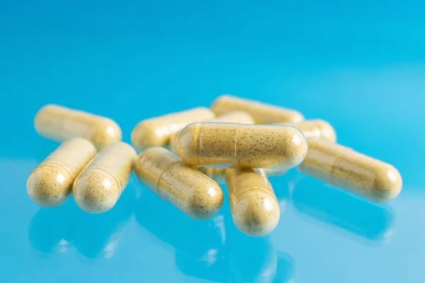 Yellow turmeric therapeutic capsules, herbal vitamin pills or drugs for treatment on blue background, medicine and healthcare concept, close-up view.