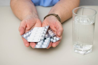 Masada kırışık yaşlı elleri olan yaşlı bir kadın. Elinde çeşitli tıbbi haplar var. Tedavi için avuç içi ilaç dolu. Sağlık ve Tıp Konsepti.