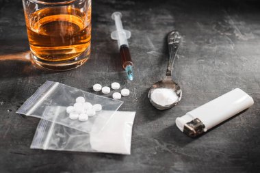 Bardakta alkol, içinde bir doz uyuşturucu olan şırınga şeffaf bir torbada beyaz haplar ve siyah arka planda bir kaşıkta uyuşturucu tozu. Bağımlılık ve kötü alışkanlıklar kavramı.