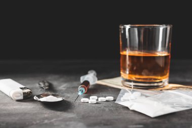 Bardakta alkol, içinde bir doz uyuşturucu olan şırınga şeffaf bir torbada beyaz haplar kaşıkta uyuşturucu tozu ve koyu arkaplanda Amerikan doları nakit. Bağımlılık ve kötü alışkanlıklar kavramı.