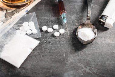 Beyaz haplar, içinde bir doz uyuşturucu bulunan şırınga kaşıkta uyuşturucu tozu ve karanlık arka planda Amerikan doları nakit para. Bağımlılık ve kötü alışkanlıklar kavramı.