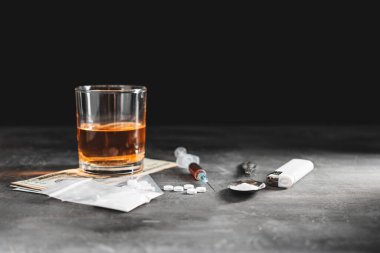 Bardakta alkol, içinde bir doz uyuşturucu olan şırınga şeffaf bir torbada beyaz haplar kaşıkta uyuşturucu tozu ve koyu arkaplanda Amerikan doları nakit. Bağımlılık ve kötü alışkanlıklar kavramı.