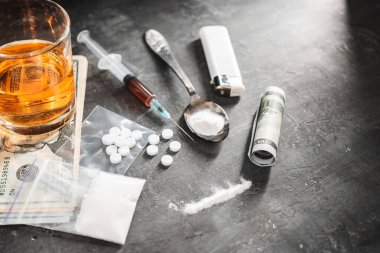 Bardakta alkol, içinde bir doz uyuşturucu olan şırınga şeffaf bir torbada beyaz haplar kaşıkta uyuşturucu tozu ve koyu arkaplanda Amerikan doları nakit. Bağımlılık ve kötü alışkanlıklar kavramı.
