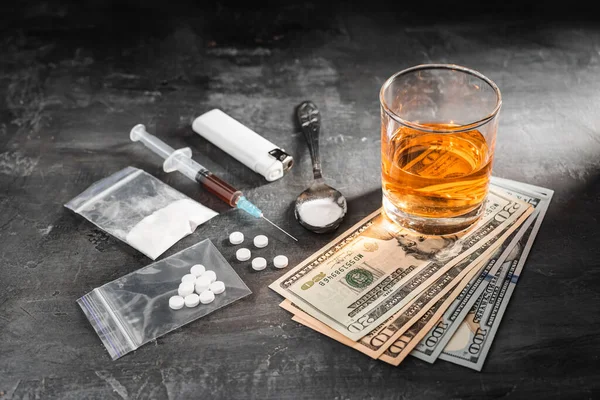 stock image Alcohol drink in a glass, syringe with a dose of drugs, white pills in a transparent bag, narcotics powder in a spoon and US dollar cash on dark background. Concept of addiction and bad habits.