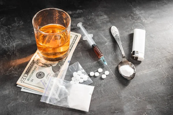 stock image Alcohol drink in a glass, syringe with a dose of drugs, white pills in a transparent bag, narcotics powder in a spoon and US dollar cash on dark background. Concept of addiction and bad habits.