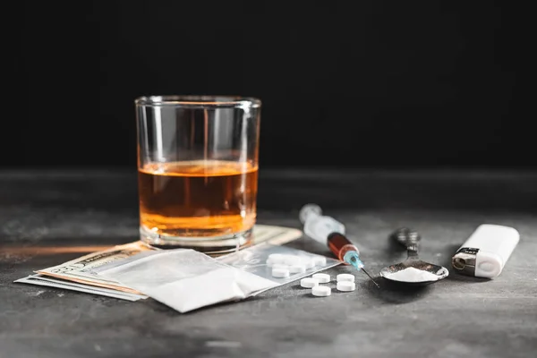 ガラスのアルコール飲料 薬の投与量の注射器 透明な袋の白い丸薬 スプーンの麻薬の粉 暗い背景の米ドルの現金 中毒や悪い習慣の概念 — ストック写真
