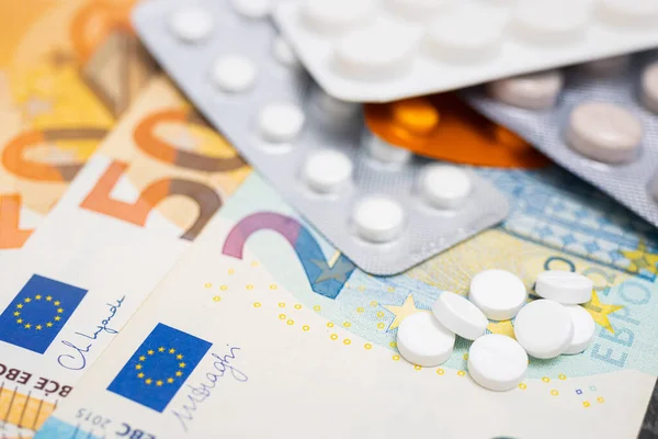 stock image White round pills, blister packs with tablets, antibiotic, painkiller or drugs and money, Euro currency banknotes, expensive medicine and healthcare concept, close-up view.