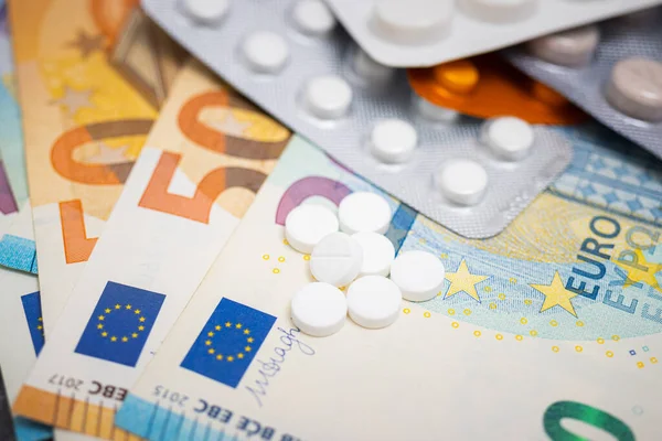 Beyaz yuvarlak haplar, tabletli su toplayıcı paketler, antibiyotik, ağrı kesici veya uyuşturucu ve para, Avrupa para birimi banknotları, pahalı ilaç ve sağlık sigortası konsepti, yakın görüş.