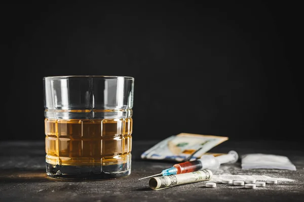 stock image Alcohol drink in a glass, syringe with a dose of drugs, white pills, narcotics powder in a transparent bag and US dollar currency cash on a dark background. Concept of addiction, abuse and bad habits.