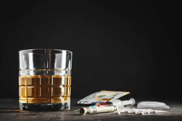 stock image Alcohol drink in a glass, syringe with a dose of drugs, white pills, narcotics powder in a transparent bag and US dollar currency cash on a dark background. Concept of addiction, abuse and bad habits.