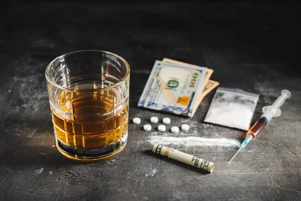 stock image Alcohol drink in a glass, syringe with a dose of drugs, white pills, narcotics powder in a transparent bag and US dollar currency cash on a dark background. Concept of addiction, abuse and bad habits.