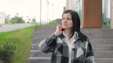 Şehir caddesinde yürüyen çekici genç bir kadın, kameraya bakıyor, ön manzara. Rüzgarlı bir bahar gününde güzel bir kızın kadın portresi.