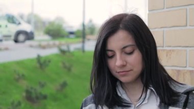 Şehir caddesinde kameraya bakan çekici bir genç kadının yakın plan portresi, akıllı telefon kullanıyor ve gülümsüyor.