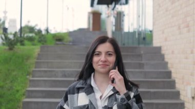 Çekici, gülümseyen genç bir kadın bir telefon alır ve şehir caddesinde yürür. Cep telefonuyla konuşan bir kadın, açık havada.