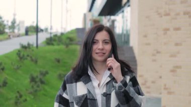 Çekici, gülümseyen genç bir kadın bir telefon alır ve şehir caddesinde yürür. Cep telefonuyla konuşan bir kadın, açık havada.