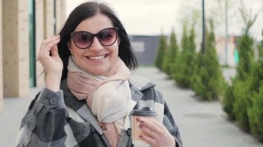Güneş gözlüklü mutlu ve hoş bir genç kadının portresi. Güzel bir gülümsemesi var. Şehirli bir caddede duruyor ve güneşli bir bahar gününde duygusal olarak komik bir hikaye anlatıyor.