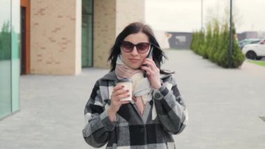 Güneş gözlüklü çekici ve hoş bir genç kadın telefon eder, kahve içer ve rüzgarlı bir bahar gününde şehir caddesinde yürür.