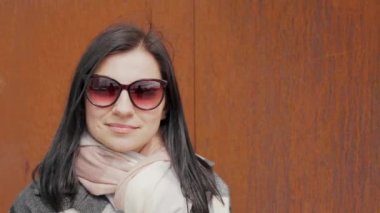 Güneş gözlüklü çekici ve hoş bir genç kadın güneşli ve rüzgarlı bir bahar gününde şehir caddesinde kahve içiyor.