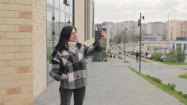 Çekici, gülümseyen genç bir kadının akıllı telefonunda bir video çağrısı var. Şehir caddesinde, cep telefonuyla konuşan bir kadın, yavaş çekim.