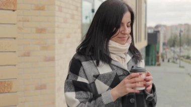 Çekici ve hoş bir genç kadın. Şehir caddesinde bir bardaktan kahve içiyor. Ağır çekimde.