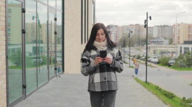 Çekici, gülümseyen genç bir kadının bir telefonu var ve şehir caddesinde yürüyor, cep telefonuyla konuşan bir kadın, ağır çekim.