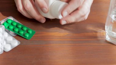 İnsan masaya ilaç ya da vitamin kapsülleri döker, manzarayı kapatır.