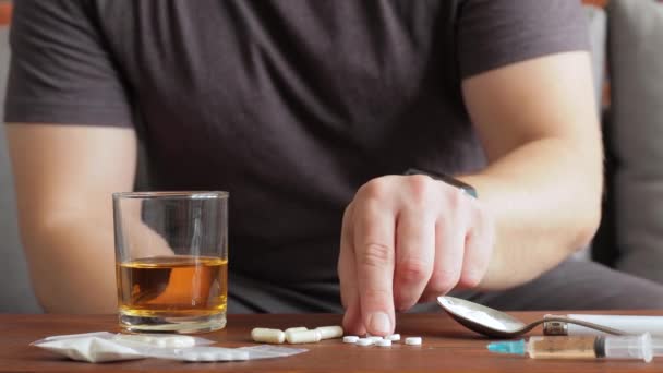 中毒の男はソファに座ってガラスからアルコールを飲んで注射器と白い粉の麻薬でテーブルの上に薬と薬を飲んで — ストック動画