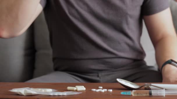 吸毒成瘾的男子坐在沙发上 喝着杯子里的酒精 在桌上用注射器和白粉吸食毒品吃药 — 图库视频影像