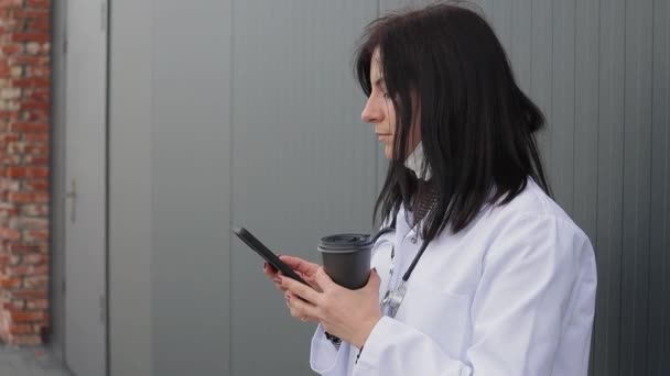 Tıbbi Maskeli Beyaz Önlüklü Akıllı Telefon Kullanan Hastanenin Arka Bahçesinde — Stok video