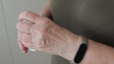 Yaşlı yetişkin bir kadın ilaç alıyor, elinde şişe tutuyor ve beyaz ağrı kesici haplar veriyor, tedavi için kapsüller, antibiyotikler veya vitaminler eski kırışık el, sağlık ve ilaç konseptine konuyor.