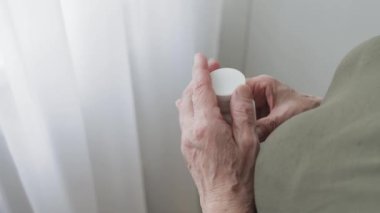 Yaşlı yetişkin bir kadın ilaç alıyor, elinde şişe tutuyor ve beyaz ağrı kesici haplar veriyor, tedavi için kapsüller, antibiyotikler veya vitaminler eski kırışık el, sağlık ve ilaç konseptine konuyor.