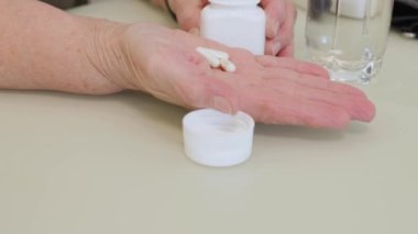 Yaşlı yetişkin bir kadın ilaç alıyor, elinde şişe tutuyor ve beyaz ağrı kesici haplar veriyor, tedavi için kapsüller, antibiyotikler veya vitaminler eski kırışık el, sağlık ve ilaç konseptine konuyor.