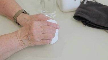 Yaşlı yetişkin bir kadın ilaç alıyor, elinde şişe tutuyor ve beyaz ağrı kesici haplar veriyor, tedavi için kapsüller, antibiyotikler veya vitaminler eski kırışık el, sağlık ve ilaç konseptine konuyor.