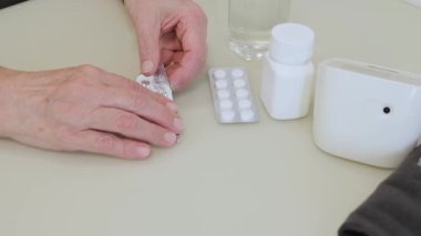 Yaşlı yetişkin bir kadın ilaç alıyor, elinde ağrı kesici haplar, tedavi için kapsüller, antibiyotikler veya kırışık el, sağlık ve ilaç konseptinde vitaminler tutuyor.