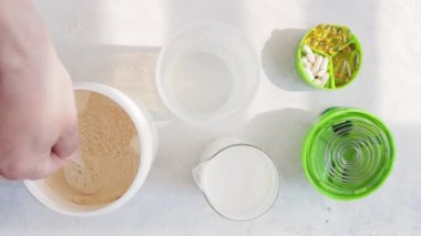 Erkek el kepçeyle beyaz süt veya soya protein tozunu bir kavanozdan plastik karıştırıcıya koyar. Protein içeceği, spor beslenmesi, üst görünüm.