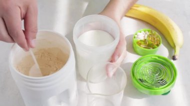 Erkek el kepçeyi beyaz süt veya soya proteini tozuyla sütle plastik karıştırıcıya koyar, muz suyu yapma süreci, spor beslenme